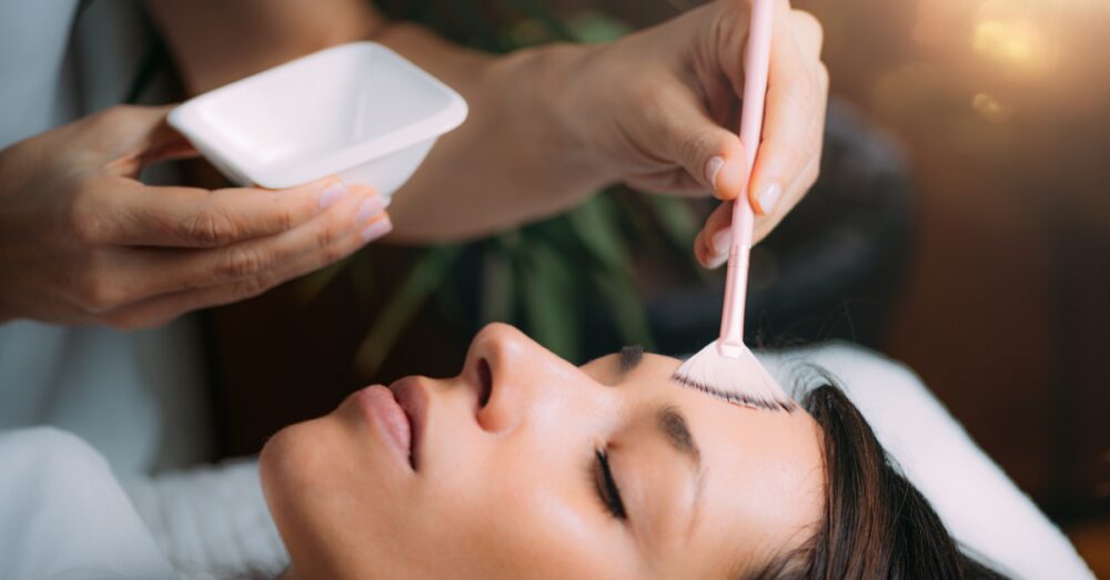 Aesthetician carefully applying VI peel solution to a woman’s face during a treatment