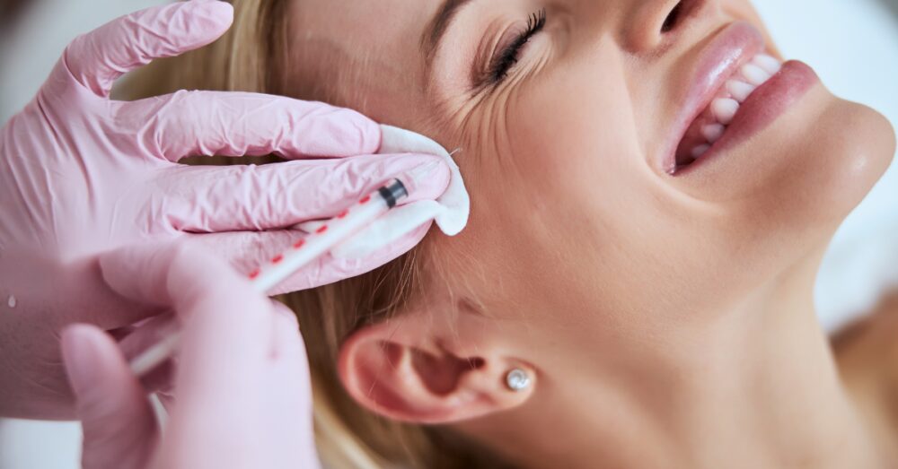 Injecting Botox near a female client's forehead and eye area to smooth crow's feet wrinkles