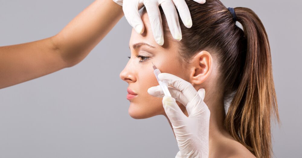 Injecting Botox near a female client's forehead and eye area to smooth crow's feet wrinkles