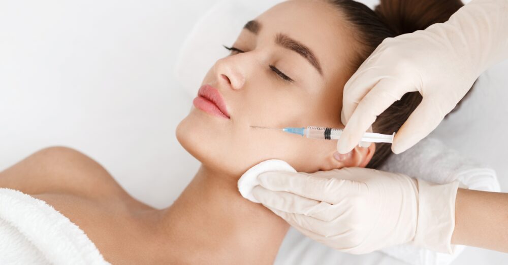 A woman receiving a Botox injection near her jawline while lying on a treatment bed in a clinical setting