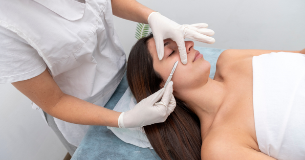 An aesthetician performing a dermaplaning procedure on a woman's face