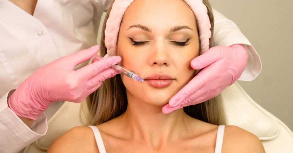 Woman with a headband receiving a lip filler injection from a provider