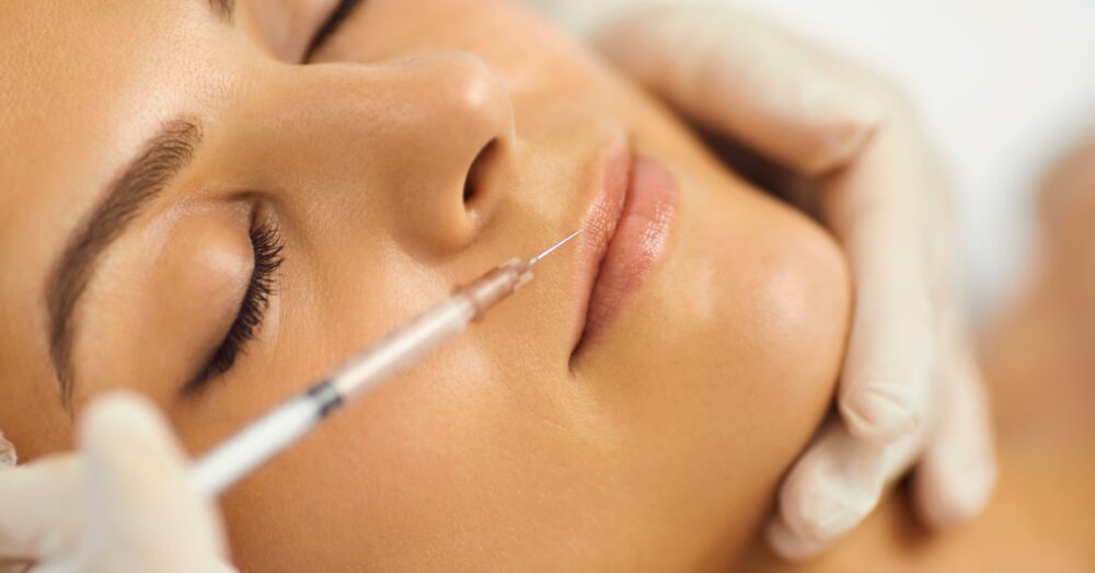 Woman lying on a treatment bed receiving a lip filler injection near the upper lip from a provider using a fine needle