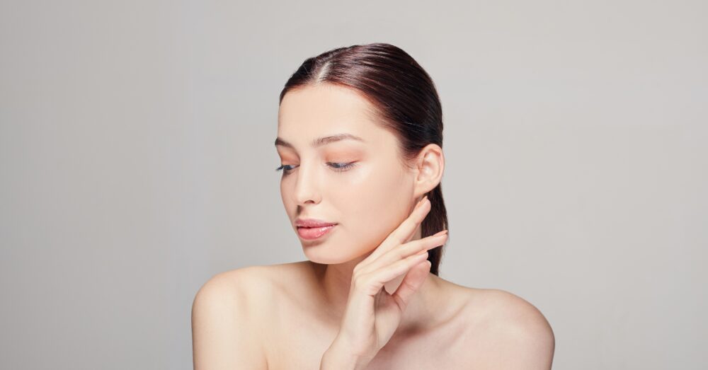 Woman with smooth skin gently touching her jawline against a neutral background